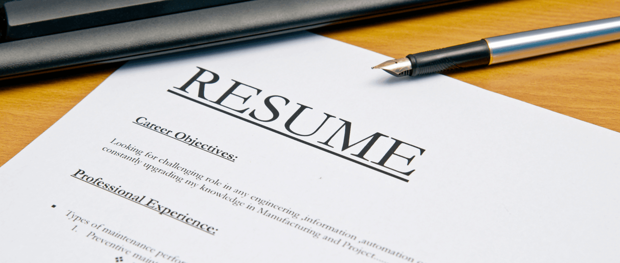 A resume under a keyboard on a wooden table