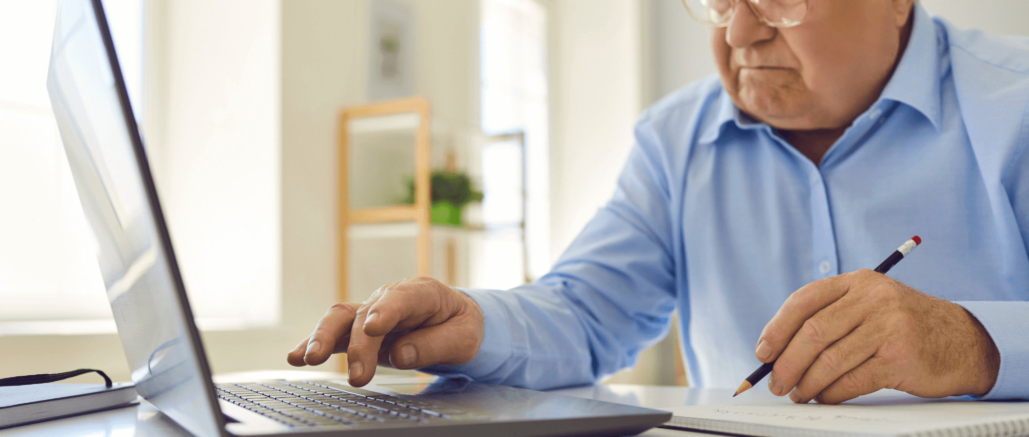 Senior using a laptop and writing notes